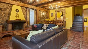 A rustic interior with a stone fireplace, wooden beams, a leather sofa, and a staircase.