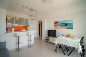 A modern kitchen with a dining area, a TV, and a painting of a beach.