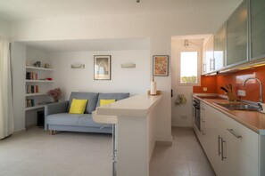 A modern kitchen with a built-in island, a grey sofa with yellow cushions, and a bookshelf.