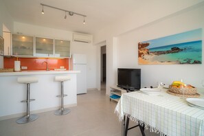 A modern kitchen with bar stools, a dining table with plates and glasses, and a painting of a beach scene.