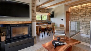 A modern kitchen with a large TV, wooden beams, stone walls, and a dining area with a fireplace.