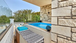 A balcony with a pool, stone wall, and a view of greenery.
