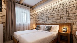 A double bed with a wooden headboard, a nightstand with a lamp, and a stone wall.