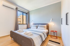 Et moderne soveværelse med en seng, et vindue, et rødt natbord og en vægmonteret lampe.