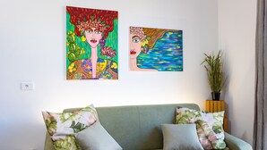 A green sofa with floral cushions, two paintings on the wall, and a potted plant. - Casa Altoliva Apartment with Shared Garden and Wi-Fi (Marsala)