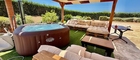 An outdoor patio with a hot tub, wooden furniture, and a pergola.
