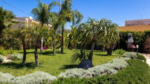 A garden with palm trees, a stone structure, and a building in the background. - Casa Altoliva Apartment with Shared Garden and Wi-Fi (Marsala)