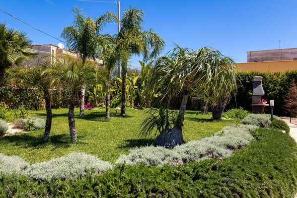 A garden with palm trees, a stone structure, and a building in the background.