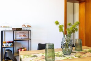 A dining table with a floral tablecloth, a glass vase with greenery, and a black chair.