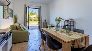 A modern kitchen with a stove, a dining table with chairs, a sofa, and a view of the outdoors. - Casa Altoliva Apartment with Shared Garden and Wi-Fi (Marsala)