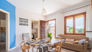 A dining area with a table, chairs, a sofa, and a view through a window.
