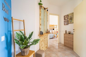 Un pasillo con pared azul, una banca de madera, una planta en maceta, un espejo y un armario de madera.