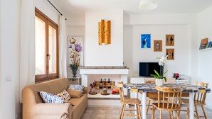 A living room with a sofa, a dining table with chairs, a fireplace, and wall art.
