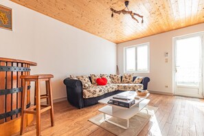 Un salon avec un plafond en bois, un canapé agrémenté de coussins à motifs, une table basse et un tabouret en bois.