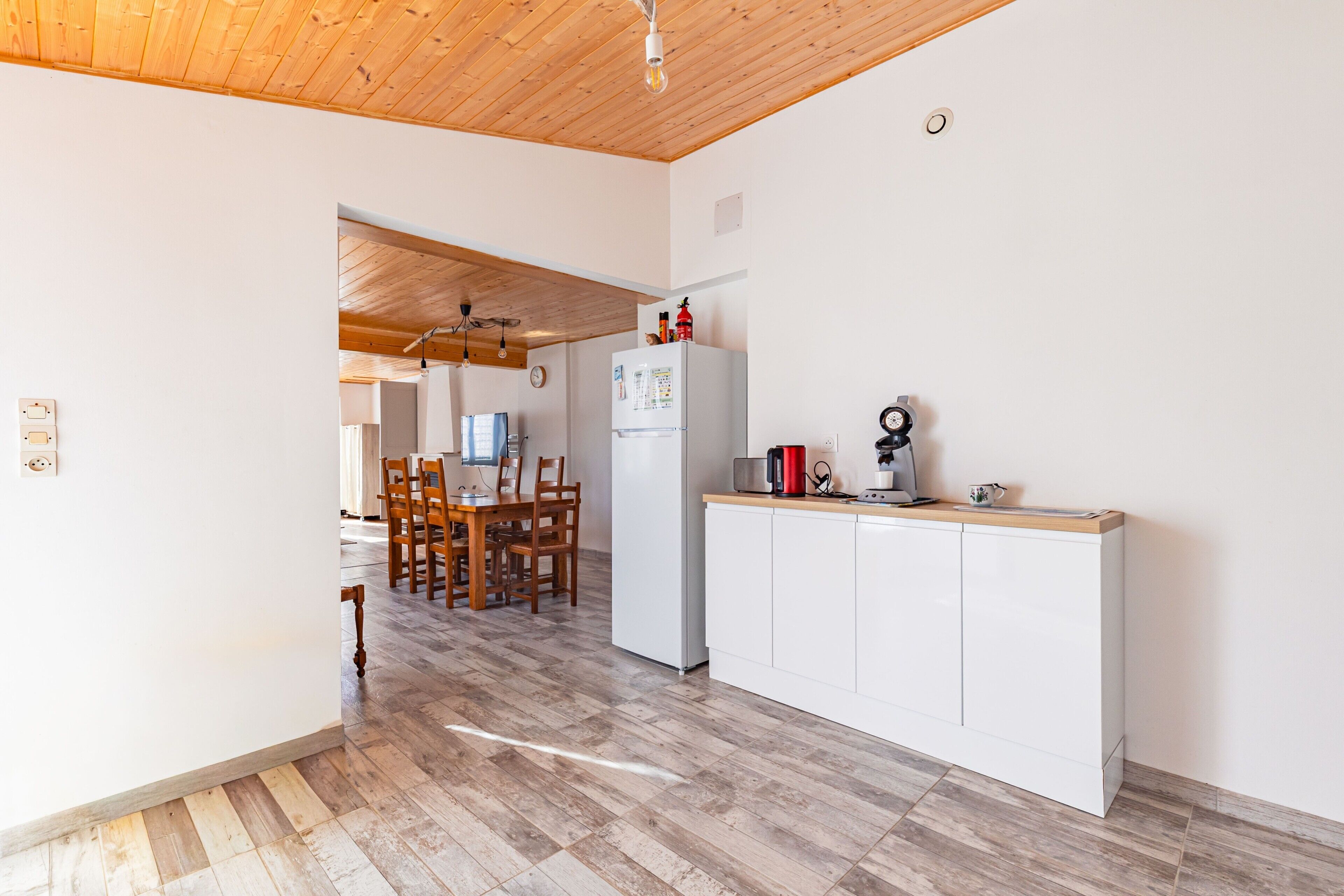 A kitchen with a wooden ceiling, white cabinets, and a dining area with wooden chairs.