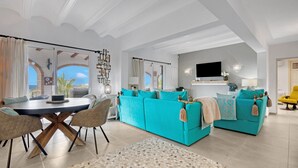 Een moderne woonkamer met een grote bank, een eettafel met stoelen en een aan de muur bevestigde televisie.