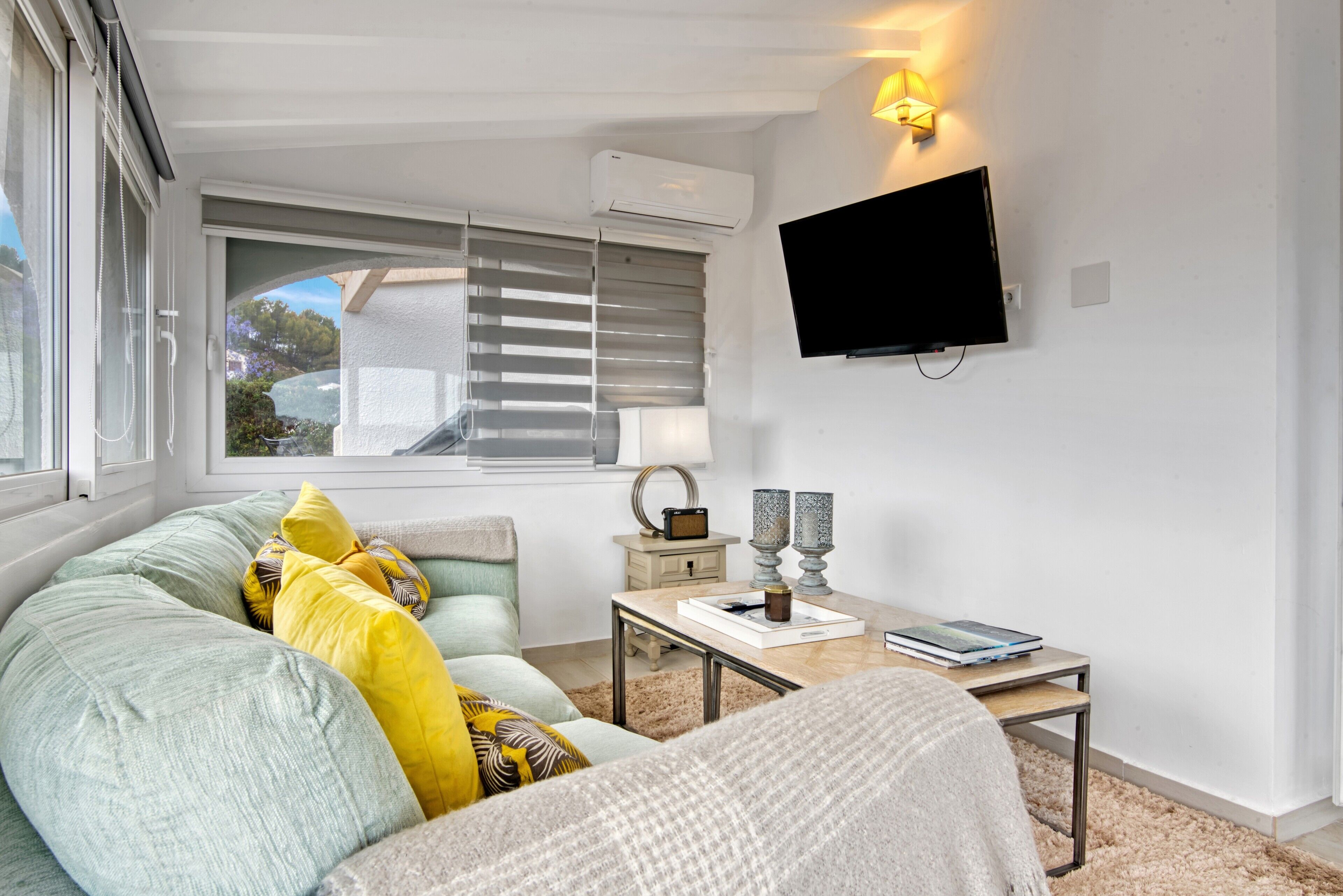 A modern living room with a sofa, a coffee table, a flat-screen TV, and a window with blinds.
