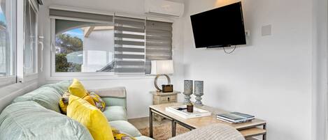 A modern living room with a sofa, a coffee table, a flat-screen TV, and a window with blinds.