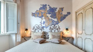 Een bed met een gestructureerde witte spreidek, twee nachtkastjes met wandlampen, en een decoratieve kaart aan de muur.