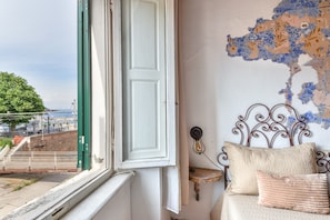 Ein Zimmer mit einem Bett, einem Fenster mit Blick auf eine Baustelle und einer Wand mit floralem Muster.