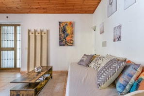 Ein Zimmer mit Holzboden, einer Couch mit gemusterten Kissen, einer Glaskugel für Fische auf einem Holztisch und einem großen abstrakten Gemälde an der Wand.