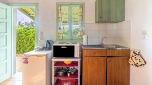 Una cocina compacta con ventana de marco verde, un refrigerador pequeño y armarios de madera.