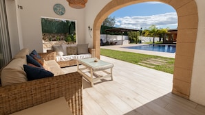 An outdoor patio with wicker furniture, a glass-top table, and a view of a swimming pool. - Villa 'Paulina' with Mountain View, Wi-Fi and Air Conditioning (Xàbia)