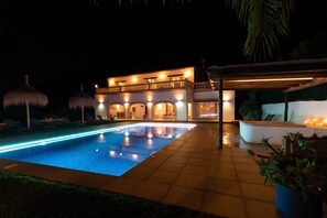 Une vue nocturne d’un hôtel doté d’une piscine, d’un espace extérieur aménagé et d’une façade bien éclairée.