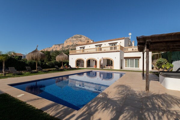 A swimming pool, lounge chairs, a white building with balconies, and a mountain in the background. - Villa 'Paulina' with Mountain View, Wi-Fi and Air Conditioning (Xàbia)