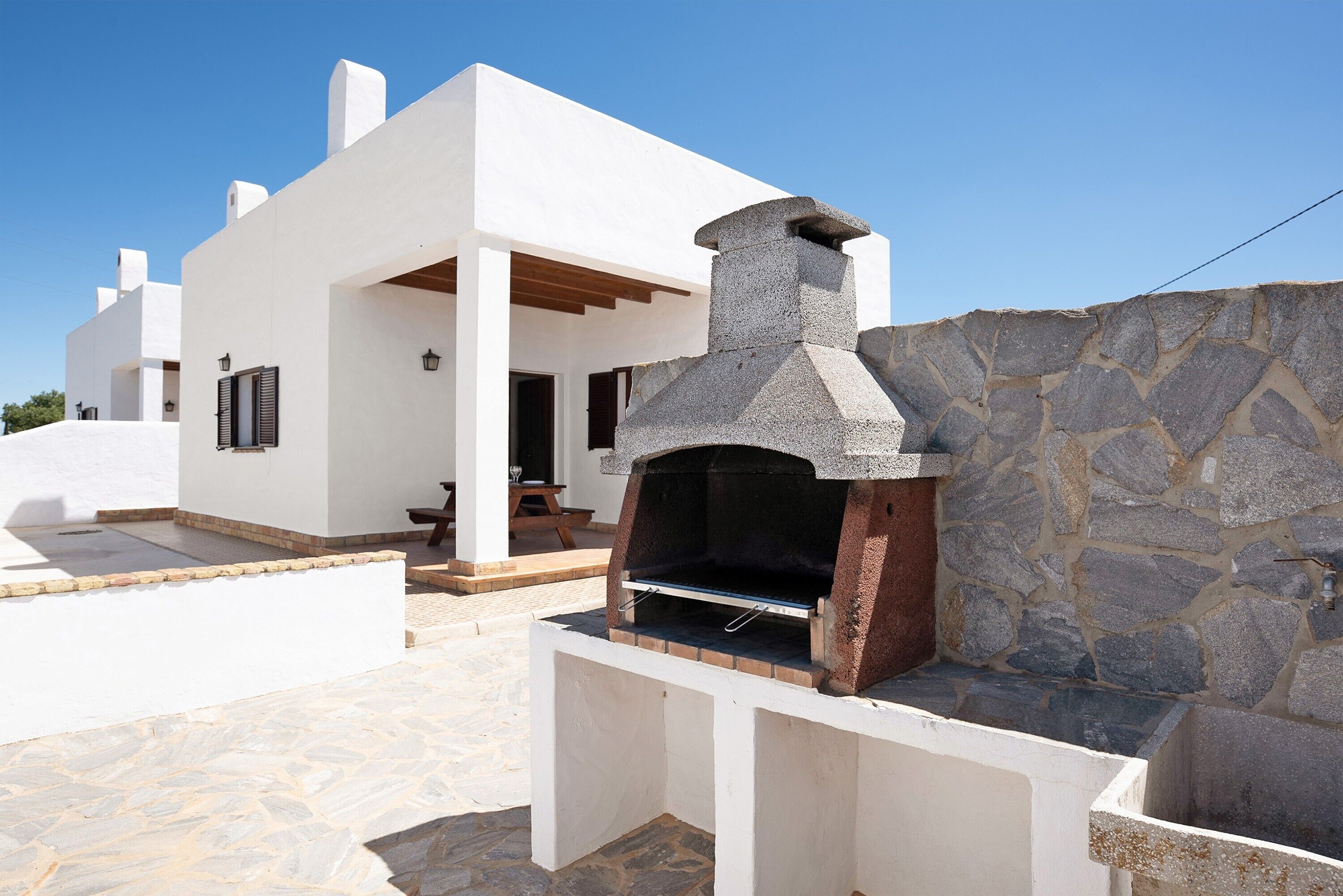 Un edificio moderno de color blanco con un horno al aire libre de piedra y un muro de piedra.