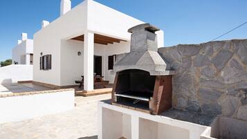 Un edificio moderno de color blanco con un horno al aire libre de piedra y un muro de piedra.