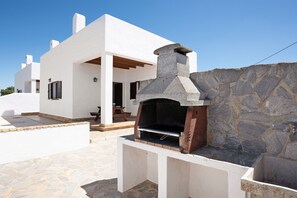 A modern white building with a stone-built outdoor oven and a stone wall.