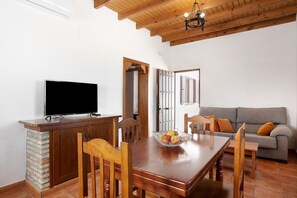 A dining area with a wooden table, chairs, a TV on a cabinet, and a gray sofa in the background. - Holiday Home 'Casa Luisa A' with Private Pool, Wi-Fi and Air Conditioning (Conil)