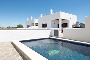A modern white building with a swimming pool, stone flooring, and a clear blue sky.
