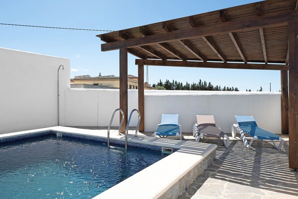 A swimming pool with a wooden pergola, lounge chairs, and a clear sky.