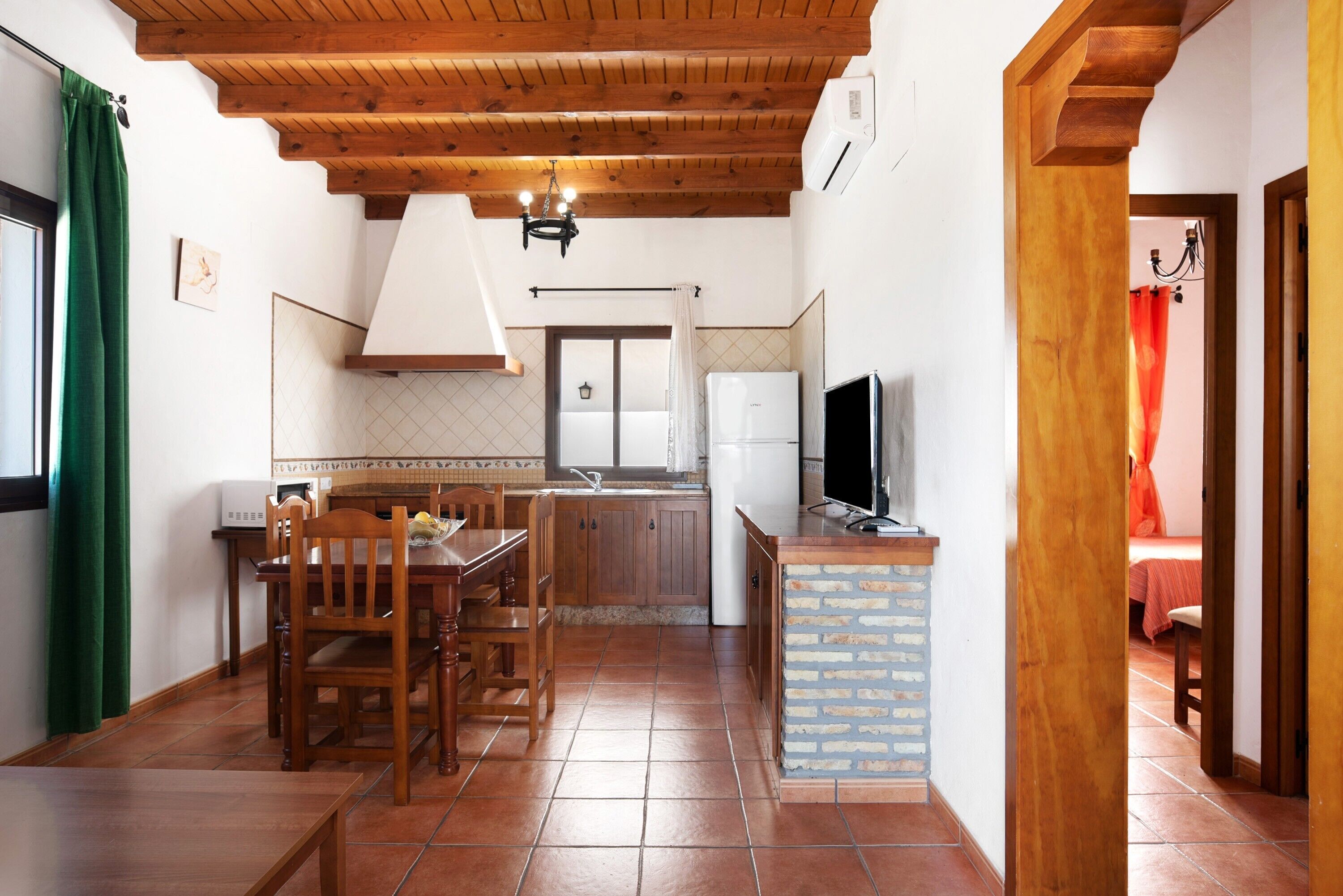 Una cocina con vigas de madera en el techo, una mesa de comedor con sillas, un refrigerador y un televisor.