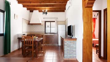Una cocina con vigas de madera en el techo, una mesa de comedor con sillas, un refrigerador y un televisor.