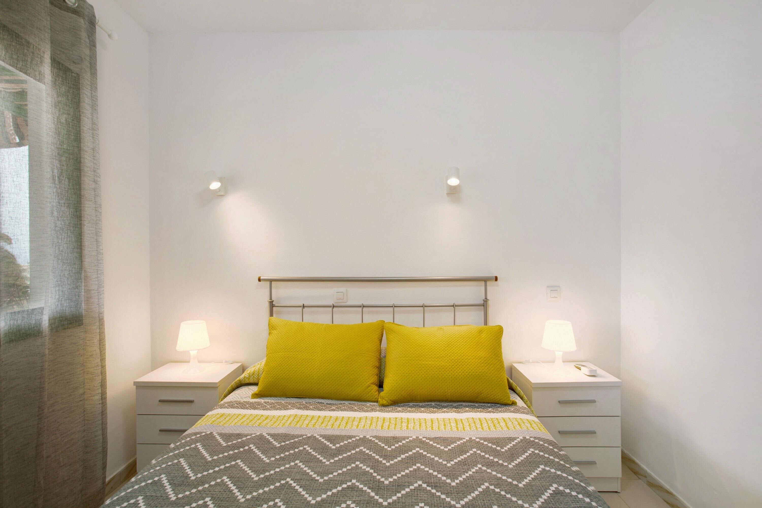 Un dormitorio con cama, dos mesitas de noche con lámparas y una ventana con cortinas.