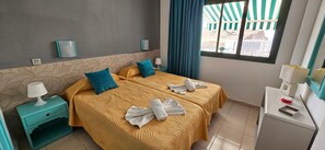 Een hotelkamer met twee bedden, een nachtkastje, een bureau en een raam met gordijnen.