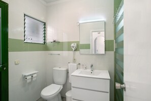 Une salle de bain avec des toilettes, un lavabo, un miroir et des murs à rayures vertes.