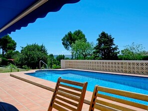 Ein Schwimmbecken mit Fliesen umrandet, zwei Holzstühle und eine Zierwand.