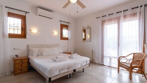 Une chambre à coucher comprenant un lit, des tables de chevet, une chaise, un ventilateur de plafond et une fenêtre avec des rideaux.