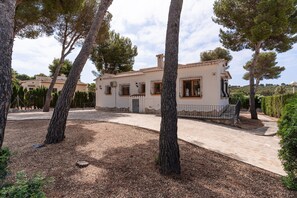 Une maison à deux étages, avec un toit en tuiles, un chemin en pierre et un jardin bien entretenu, agrémenté d’arbres.