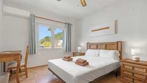 A bedroom with a bed, a desk, a chair, a nightstand, and a window with curtains. - Villa 'Cristina' with Mountain View, Wi-Fi and Air Conditioning (Xàbia)