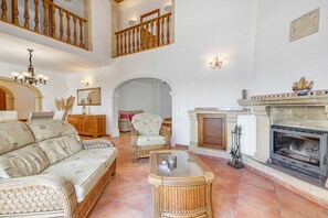 A spacious living room with a high ceiling, a fireplace, a sofa, a chair, and a glass coffee table. - Villa 'Cristina' with Mountain View, Wi-Fi and Air Conditioning (Xàbia)
