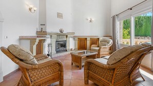 A spacious living area with wicker furniture, a fireplace, and large windows offering a view of greenery. - Villa 'Cristina' with Mountain View, Wi-Fi and Air Conditioning (Xàbia)