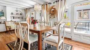 A dining area with a wooden table, white chairs, a chandelier, and a view through a glass door. - Villa 'La Siesta' with Mountain View, Private Pool and Wi-Fi (Xàbia)
