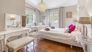 A bedroom with a bed, bedside tables, a desk, a chair, a bench, and a window. - Villa 'La Siesta' with Mountain View, Private Pool and Wi-Fi (Xàbia)