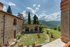 Un edificio de piedra con un patio, plantas en macetas y vistas a un paisaje montañoso.