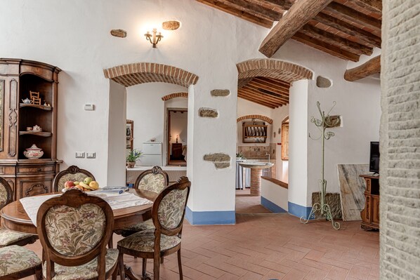 Un comedor con una mesa y sillas de madera, una cocina al fondo y detalles de piedra en las paredes.